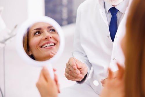 woman looking at her smile in hand mirror